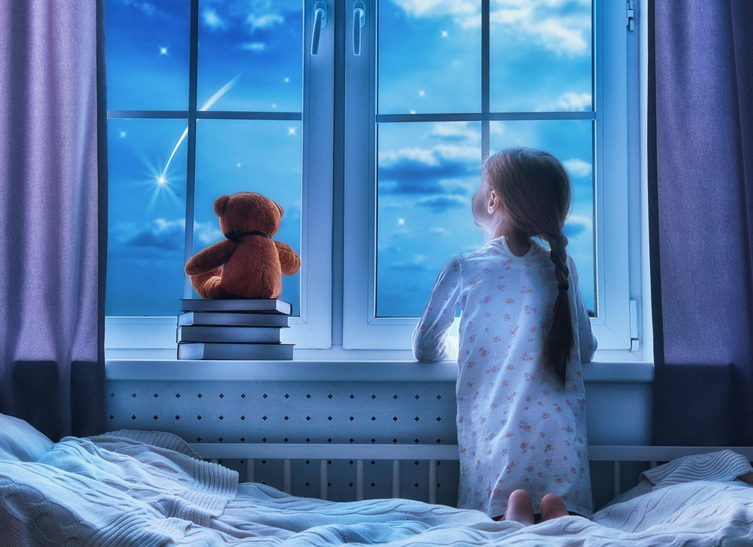 A little girl is sitting in bed looking out the window.