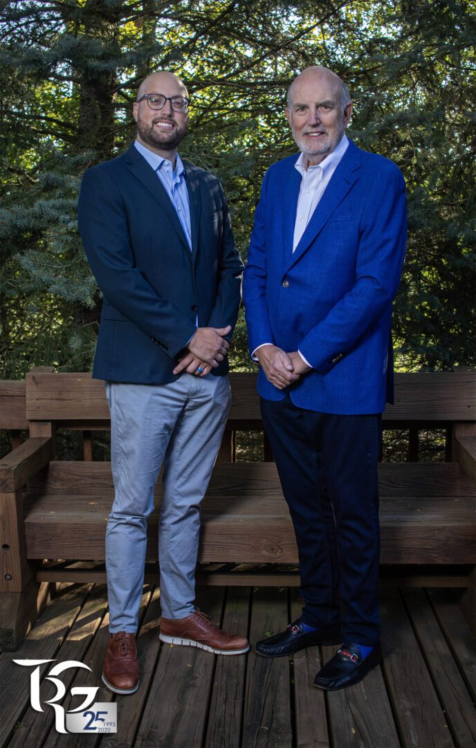 Two men standing on a wooden bench in the woods.